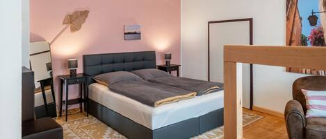 A bedroom with a bed, bedside tables, a chair, a rug, and a painting on the wall.