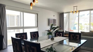 Et moderne spiseområde med et glasbord, stole og hængende lys.