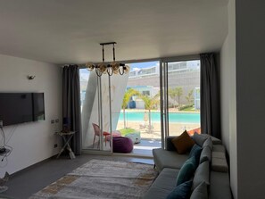 Ein modernes Wohnzimmer mit großem Fernseher, einer Couch, einem Couchtisch und Blick auf Pool und Strand.