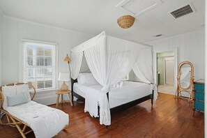Ein Schlafzimmer mit einem Himmelbett, einer Tagesliege, einem kleinen Tisch mit Lampe und einem Spiegel.
