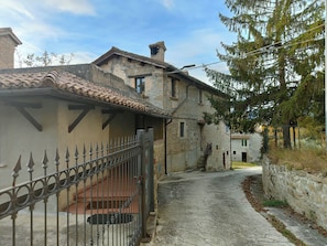 Une ruelle étroite, avec un bâtiment en pierre, une clôture en métal et un arbre sur la droite.