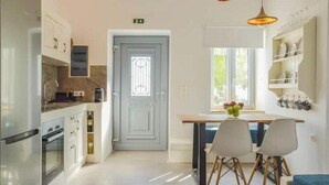 Une cuisine moderne avec des armoires blanches, un four encastré, un coin repas avec une table et des chaises, et une fenêtre offrant une vue agréable.