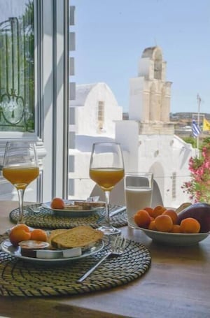 A breakfast table with glasses of orange juice and milk, a plate with bread and fruit, and a bowl of oranges.