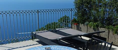 Ein runder Tisch mit blauer Mosaikplatte, zwei Stühle und Blick aufs Meer.
