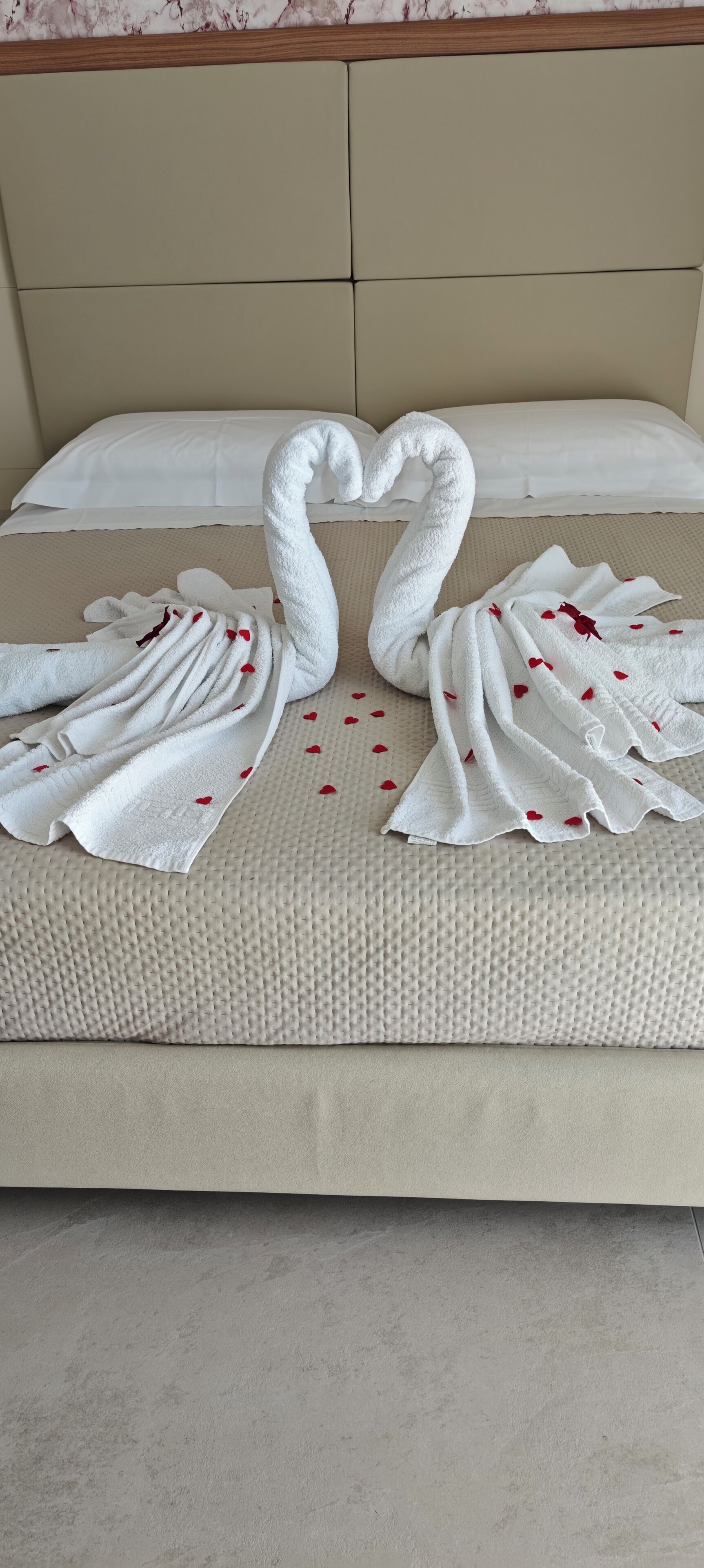 Een bed met hoofdeinde, een witte spreideken en twee handdoeken gevouwen in de vorm van een zwaan, versierd met rode hartjes.
