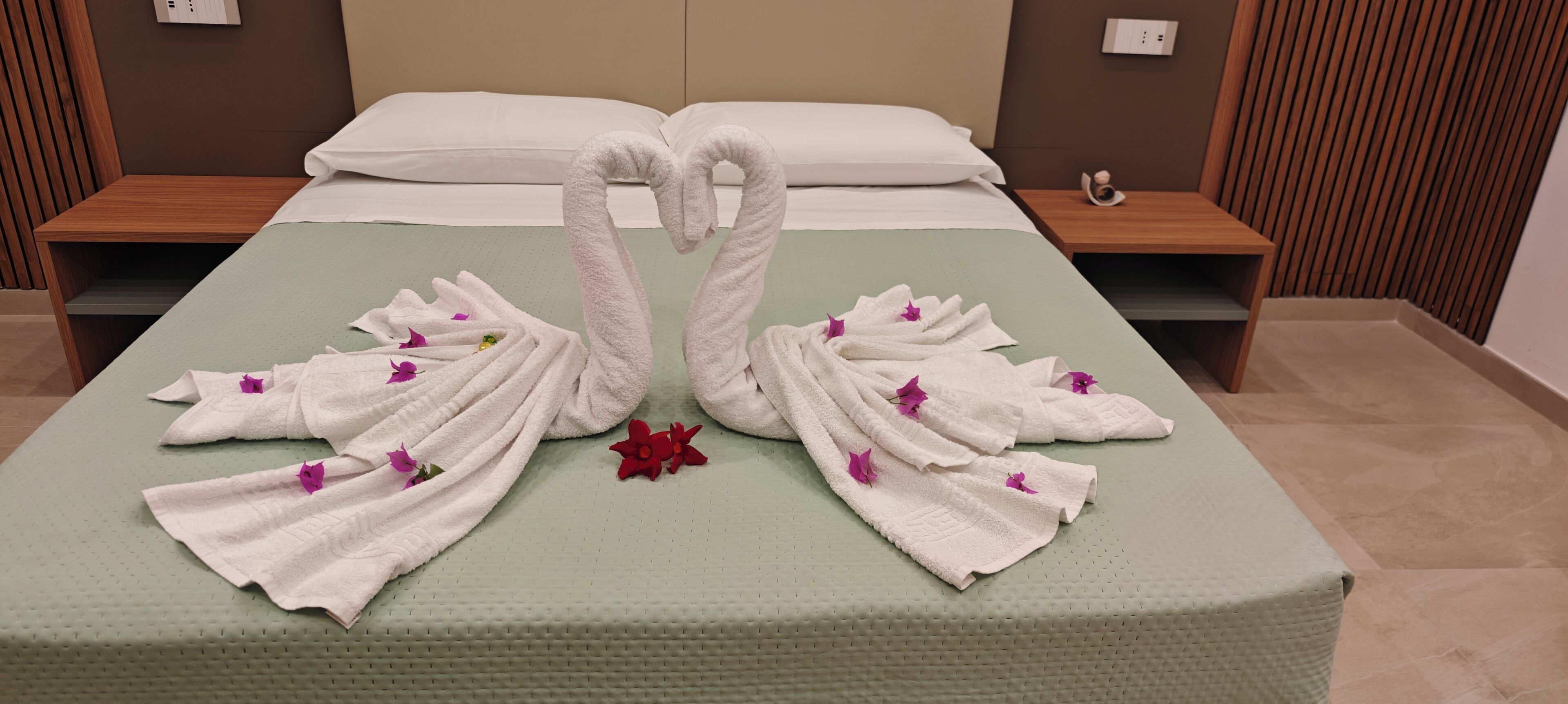 A hotel room with a bed, two wooden nightstands, and a wall-mounted power outlet.