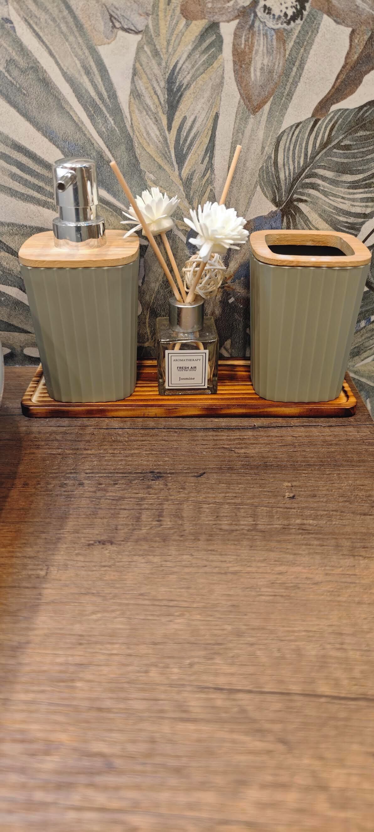 A wooden tray with a diffuser, a small vase with white flowers, and a container with a label.