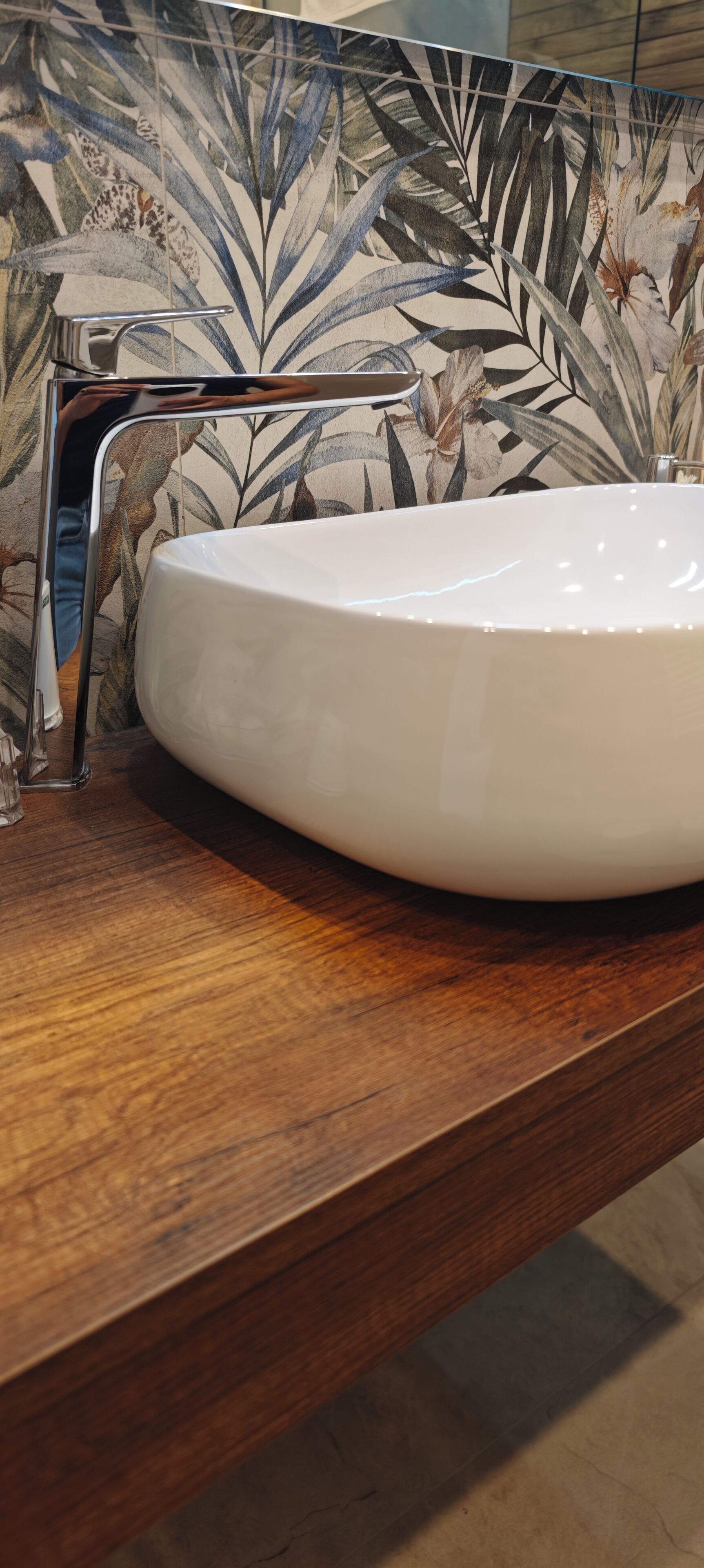 Un bagno con un lavandino bianco, un piano d'appoggio in legno e un rubinetto metallico.
