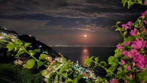 A coastal view with a moonlit sea, a bridge, and a lit-up cityscape in the distance. - Al Chiar di Luna - Furore (Furore)
