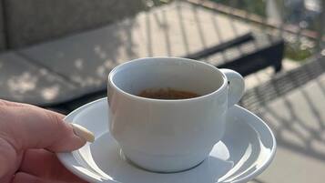 Una mano sostiene una taza blanca de café sobre un platito, con un fondo exterior desenfocado.