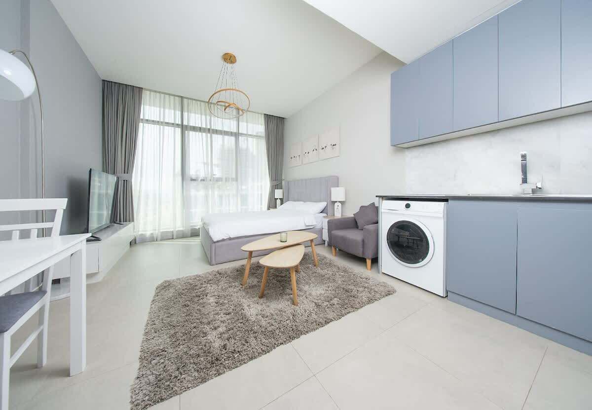 Habitación de hotel moderna con cama, escritorio, lavadora y zona de comedor.