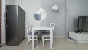 Een moderne keuken met een geïntegreerde koelkast, een eettafel met stoelen, een ronde spiegel, een vloerlamp en een televisie op een wit kastje.