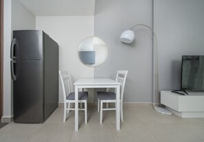 A modern kitchen with a built-in refrigerator, a dining table with chairs, a round mirror, a floor lamp, and a TV on a white cabinet. - Studio w/ Pool & Gym at JVC Living Garden (Dubai)