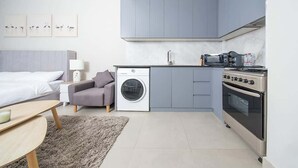 Een compacte hotelkamer met een bed, een slaapbank, een wasmachine, een kitchenette met een kookplaat en een klein tafeltje.