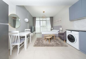 A modern, compact living space with a dining area, a sofa, a bed, and a washing machine.