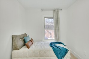 A bedroom with a bed, pillows, a blanket, a window with curtains, and a view of a building outside. - Modern 3BR Apartment: 4 Bed, 2 Bath, 2 Floors, Games & BBQ (Cambridge)