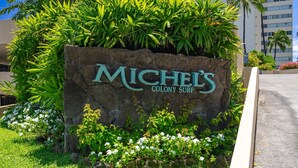 A sign for 'MICHELE'S COLONY SURF' with lush greenery and white flowers around it. - Oceanfront Gold Coast with Full Ocean & Diamond Head Views! Free Parking! (Honolulu)