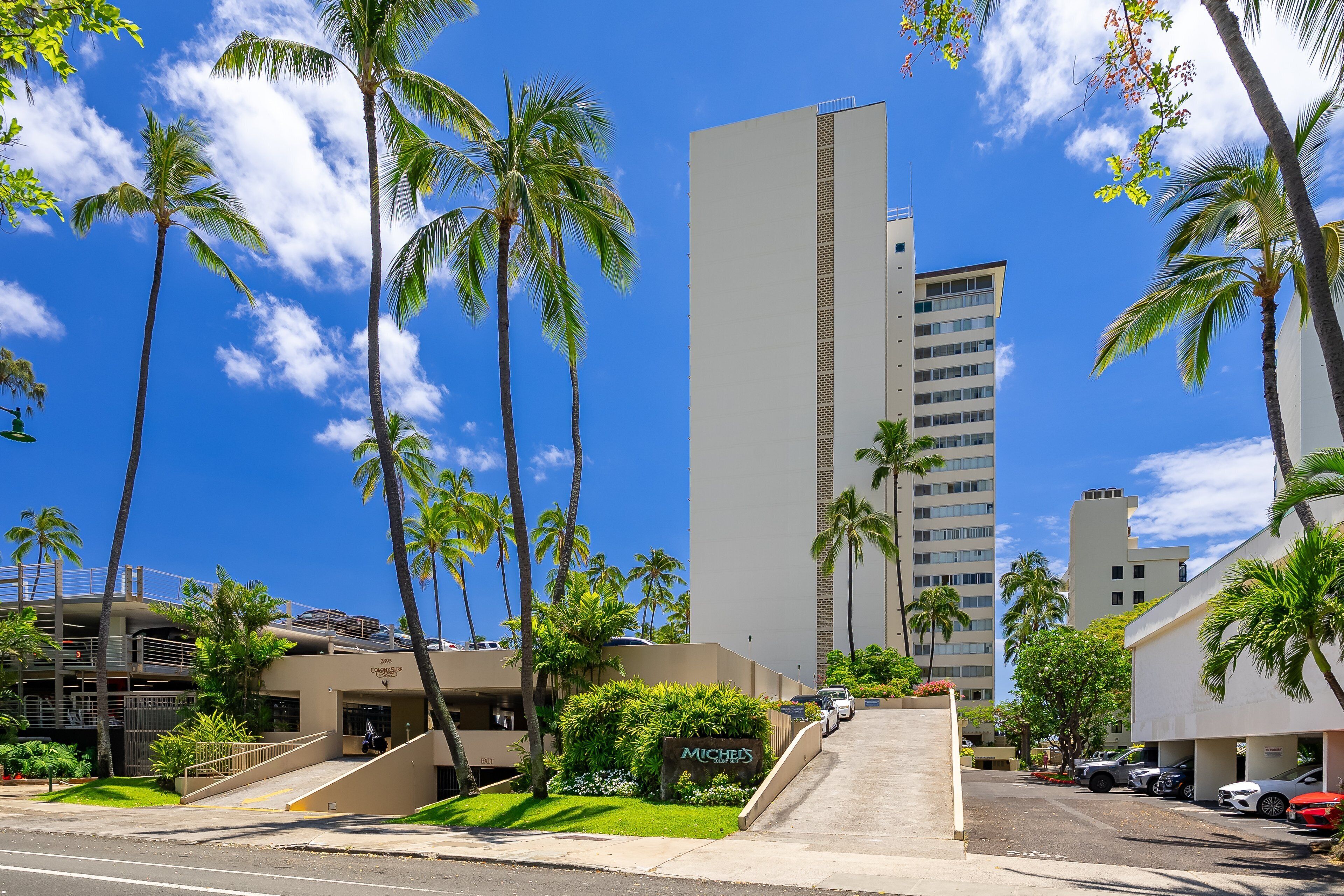 A hotel with a modern design, palm trees, and a clear blue sky.