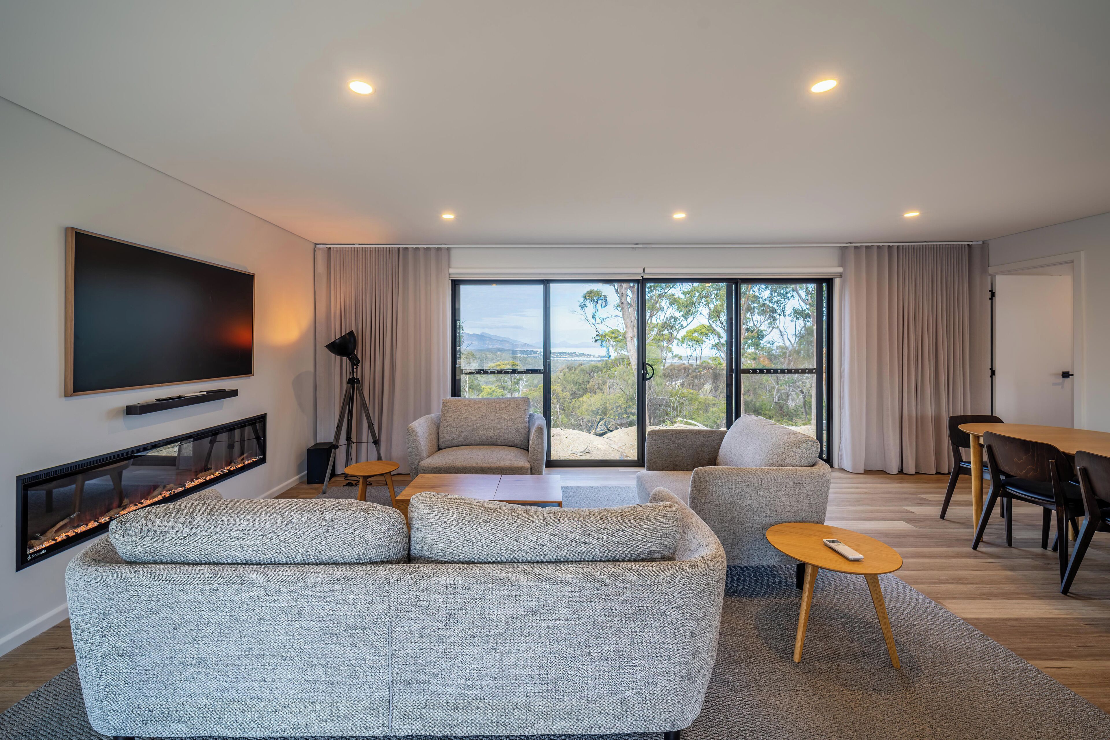 A modern living room with a fireplace, a flat-screen TV, a sofa, a coffee table, and a dining area with chairs.