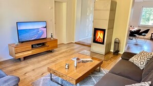 A modern living room with a TV, a fireplace, a sofa, and a coffee table. - Family home near Darß—fireplace, patio, and plenty of space surrounded by nature (Pruchten)