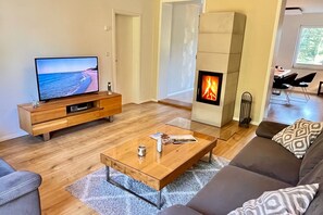 A modern living room with a TV, a fireplace, a sofa, and a coffee table. - Family house near Darß - fireplace & terrace, quiet location, tastefully furnished. (Pruchten)