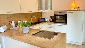 A modern kitchen with white cabinets, a stainless steel range hood, a built-in oven, a microwave, and a coffee maker. - Family home near Darß—fireplace, patio, and plenty of space surrounded by nature (Pruchten)