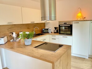 A modern kitchen with white cabinets, a stainless steel range hood, a built-in oven, a microwave, and a coffee maker. - Family house near Darß - fireplace & terrace, quiet location, tastefully furnished. (Pruchten)