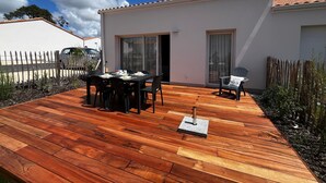 A patio with a table and chairs, a small outdoor seating area, and a building with a tiled roof. - House between forest and beach - 4 guests (Saint-Jean-de-Monts)