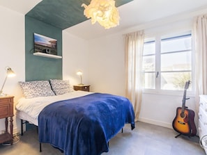 Ein Schlafzimmer mit einem Bett, Nachttischlampen, einer Gitarre, einem Fenster mit Vorhängen und einem Bild an der Wand.