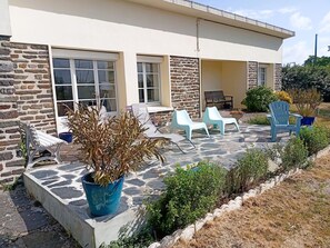 Un bâtiment aux murs en pierre, doté de grandes fenêtres et d’une terrasse avec des sièges extérieurs.
