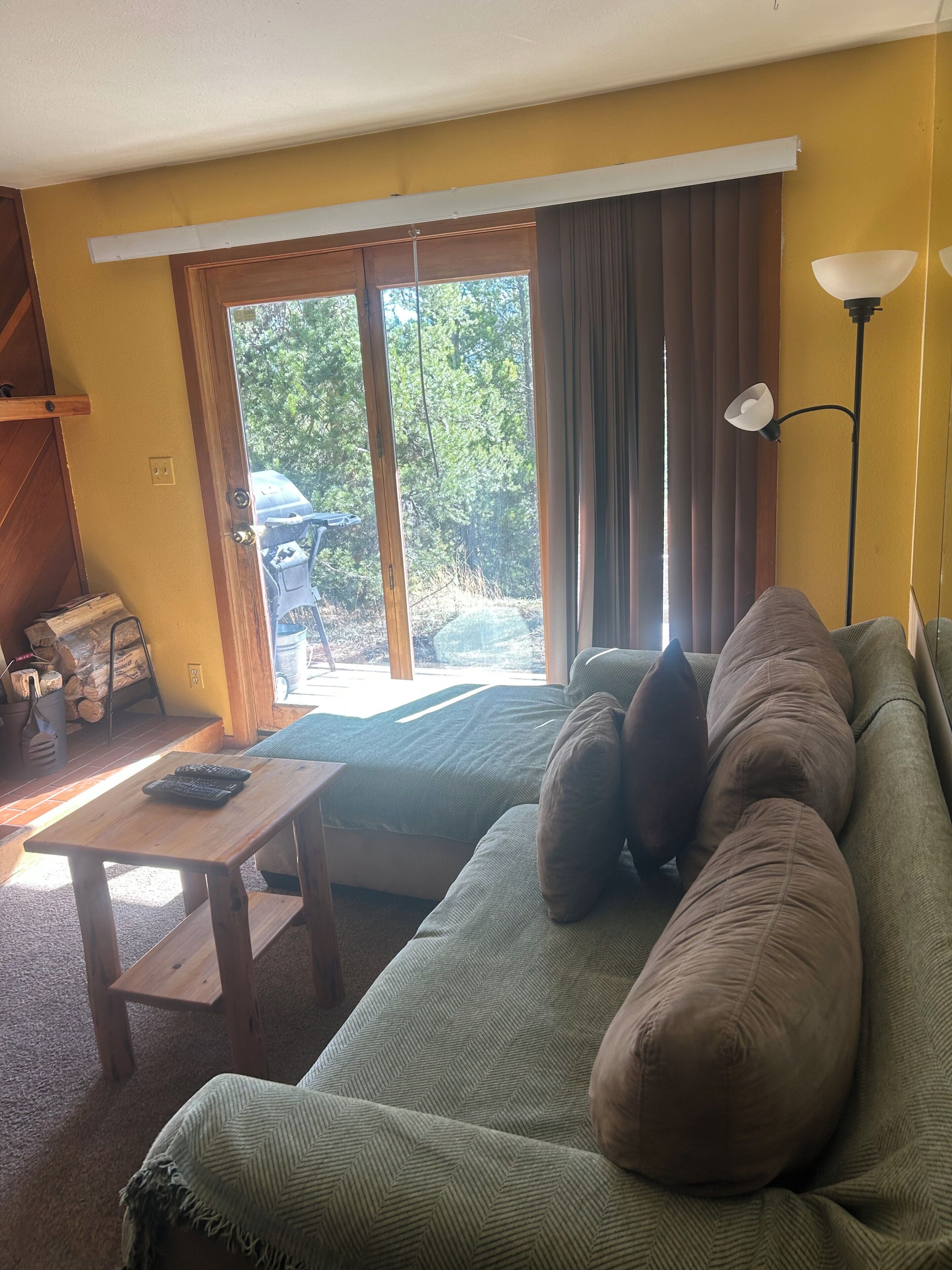 A living room with a green sofa, a wooden coffee table, a lamp, and a view through a large window.
