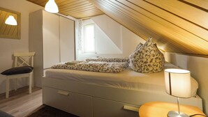 A bedroom with a sloped ceiling, a bed with patterned bedding, a bedside lamp, a chair, and a window.