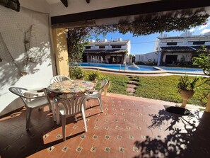 Eine Terrasse mit Tisch und Stühlen, ein Schwimmbad und traditionelle Gebäude im Hintergrund.