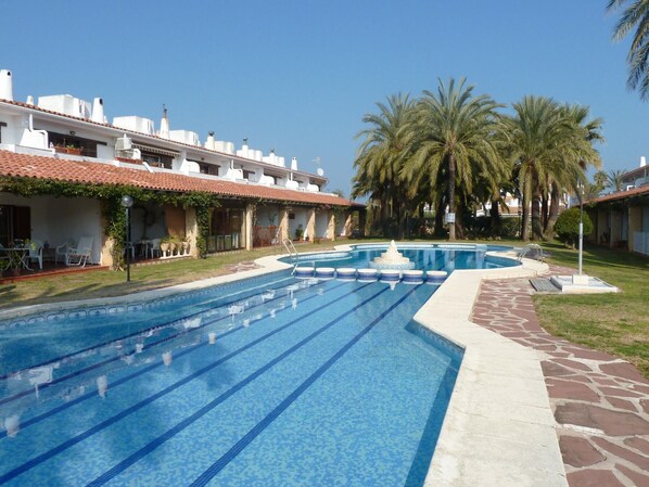 Ein Swimmingpool mit einer Fontäne, umgeben von Palmen und einem Gebäude mit einem Ziegeldach.
