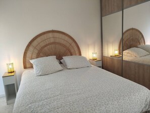 Ein Schlafzimmer mit einem großen Bett, zwei Nachttischen, einem Spiegel und einem an der Wand befestigten Kopfteil.