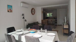 Ein Essbereich mit Tisch für vier Personen, eine Küche im Hintergrund und ein Wohnbereich mit Sofa und Couchtisch.