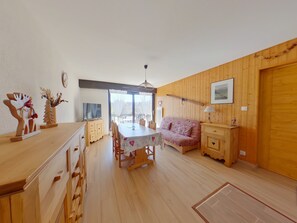 A cozy room with a wooden floor, a dining table with chairs, a sofa, and a TV. - Charming apartment - 4 guests (Les Rousses)