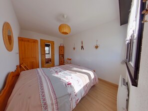 A bedroom with a wooden bed, a door, a mirror, a hanging light fixture, and a window with curtains. - Charming apartment - 4 guests (Les Rousses)