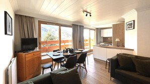 Un'accogliente zona giorno con TV, mobili in legno, un tavolo da pranzo e angolo cottura.