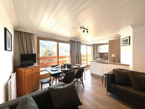 Una sala de estar acogedora con televisor, muebles de madera, una mesa de comedor y una zona de cocina.