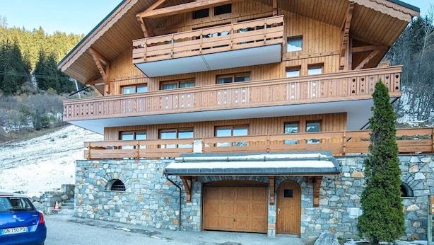 Una baita a più piani in legno, con balconi, fondamenta in pietra e un garage.