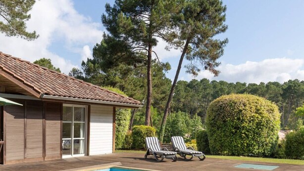 A swimming pool with lounge chairs, a wooden deck, and a building with shutters. - Villa with pool, pets allowed - 6 guests (Moliets-et-Maa)