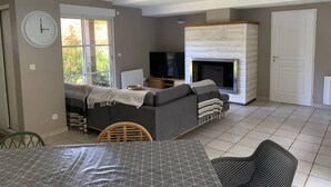 A living room with a sofa, TV, fireplace, and a dining area with a table and chairs. - Villa with pool, pets allowed - 6 guests (Moliets-et-Maa)