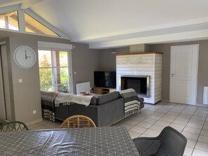 A living room with a sofa, TV, fireplace, and a dining area with a table and chairs. - Villa with pool, pets allowed - 6 guests (Moliets-et-Maa)