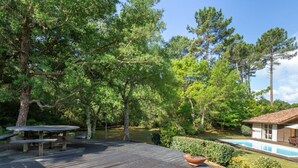 A wooden deck with a picnic table, surrounded by trees and a swimming pool. - Villa with pool, pets allowed - 6 guests (Moliets-et-Maa)