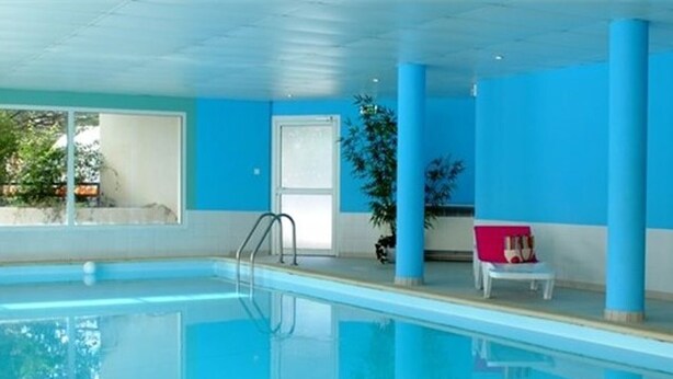 Una piscina interior con agua azul cristalina, una escalera y una silla con cojín rojo.
