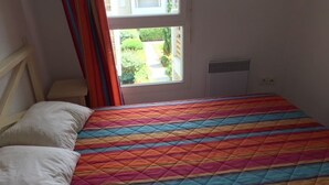 Una habitación con cama, ventana con cortinas, radiador y una pequeña mesa.