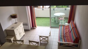 Una habitación con una mesa de comedor, sillas, un sofá, un armario y un ventanal corredero que da a un espacio exterior con césped y mobiliario de patio.