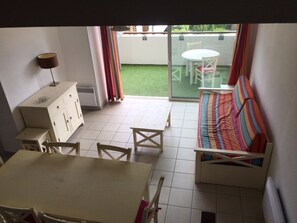 Ein Zimmer mit Esstisch, Stühlen, einer Couch, einem Schrank und einer Schiebetür zu einem Außenbereich mit Rasen und Terrassenmöbeln.