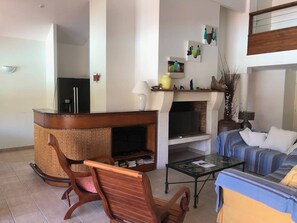 Ein Wohnzimmer mit Kamin, einer Couch, einem Couchtisch und einem Korbstuhl.
